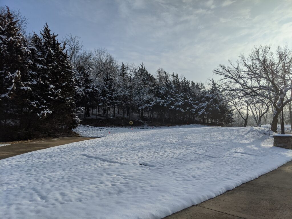 Snow-covered landscape with a cleared path, sunlit trees, and a mostly clear sky.